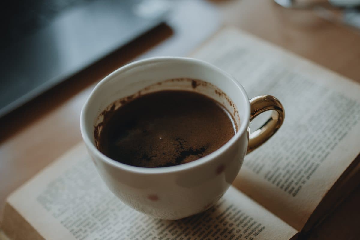 A warm cup of coffee resting on an open book on a wooden desk — a cozy start to learning French